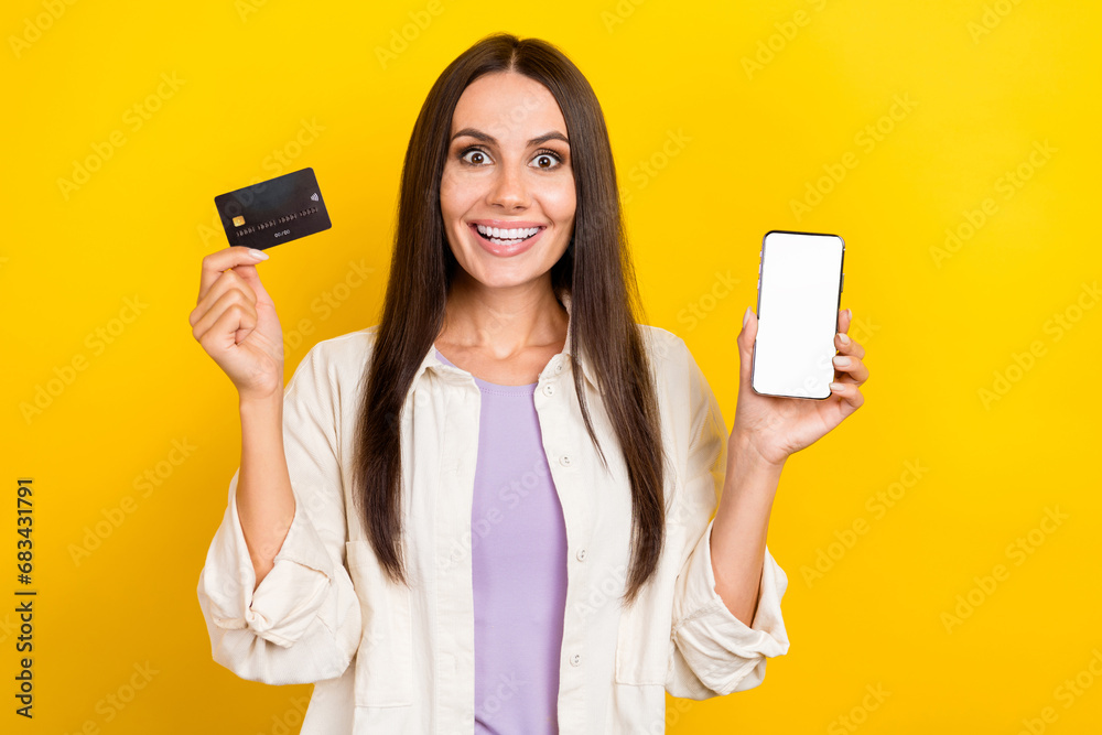 Portrait of excited girl wear shirt presenting smartphone touchscreen empty space hold credit card isolated on yellow color background Portrait of excited girl wear shirt presenting smartphone touchscreen empty space hold credit card isolated on yellow color background