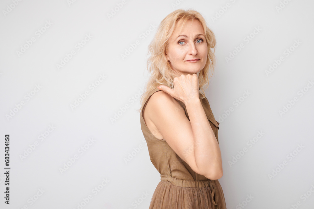 Fototapeta premium Beautiful mature woman 50 years old pointing finger aside, demonstrating empty space for product or text isolated on white studio background