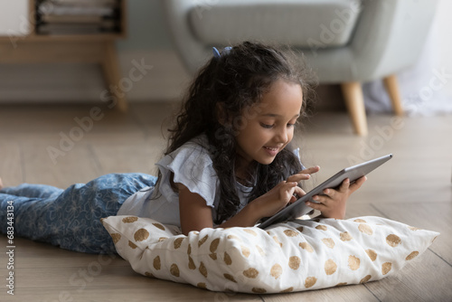 Cute little Indian girl using digital tablet, play video games on-line, spend time on internet alone at home. Generation Alpha and modern wireless tech, parental control software, apps usage concept photo