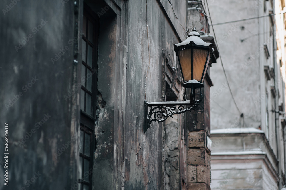 Medieval metal black street lamp on the wall along a winter street in Lviv. Vintage retro lantern on the facade of a house covered with snow.