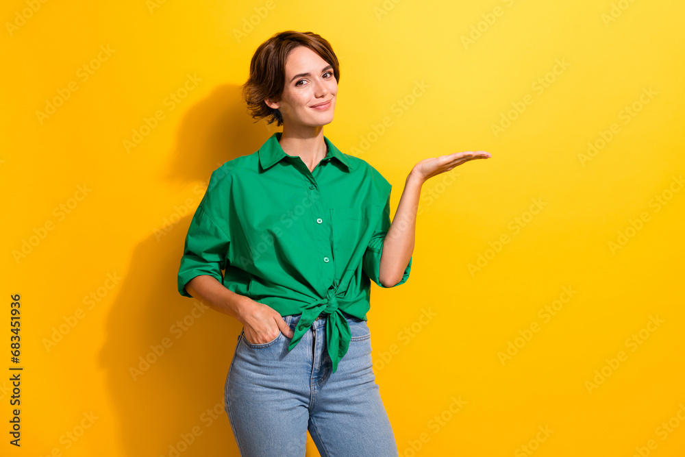 Photo of positive cute girl dressed green shirt showing arm empty space isolated yellow color background Photo of positive cute girl dressed green shirt showing arm empty space isolated yellow color background