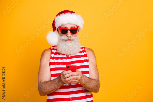 Photo of cool positive senior guy christmas swimwear hat glasses communicating device empty space isolated yellow color background