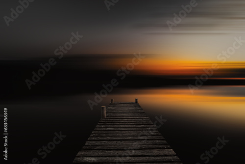 Old wooden boardwalk, dock in lake with abstract blurred background in dark evening. Abstract blurred sunset background