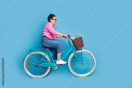 Full length photo of overjoyed excited woman dressed pink blouse riding bicycle look at empty space isolated on blue color background © deagreez