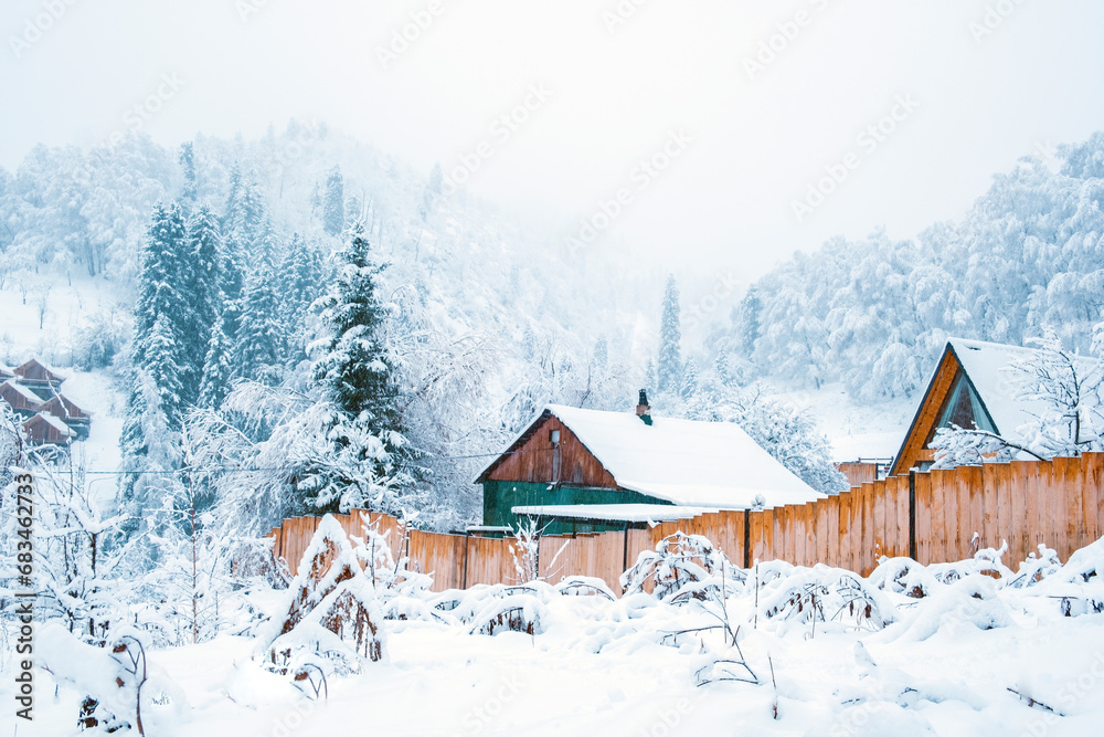 Naklejka premium Winter village at the foot of the snowy mountains in winter fairy tale during snowfall