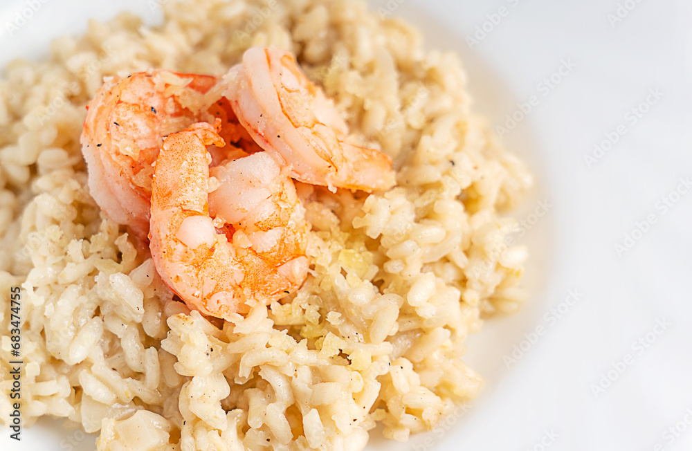 Close up view of creamy homemade traditional italian risotto dish made of fried and boiled arborio rice cooked with broth decorated with shrimps or prawns seafood and parmesan cheese served in plate