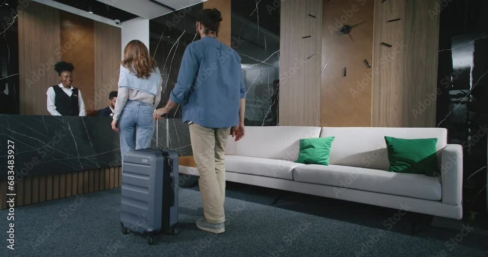 Lovely beautiful couple walking to hotel's reception desk where male and female receptionists waiting to greet visitors. Professional experienced nice hotel workers helping guests check in.