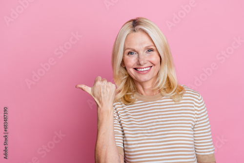 Photo of good mood person with blond hairstyle dressed striped t-shirt indicating at sale empty space isolated on pink color background