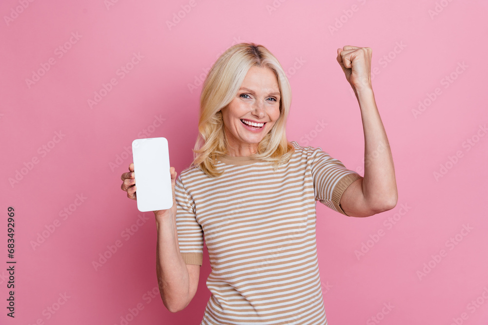 Portrait of delighted person raise fist achievement show empty space smart phone screen isolated on pink color background Portrait of delighted person raise fist achievement show empty space smart phone screen isolated on pink color background