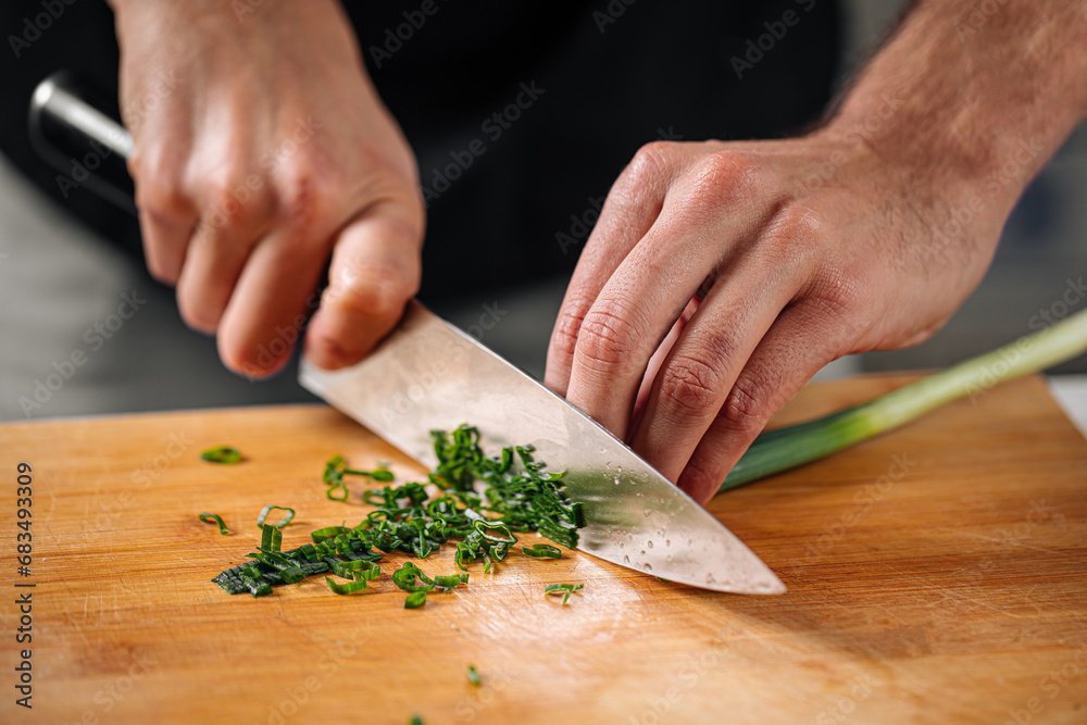 Chef chopping spring onion on wooden cutting board Chef chopping spring onion on wooden cutting board