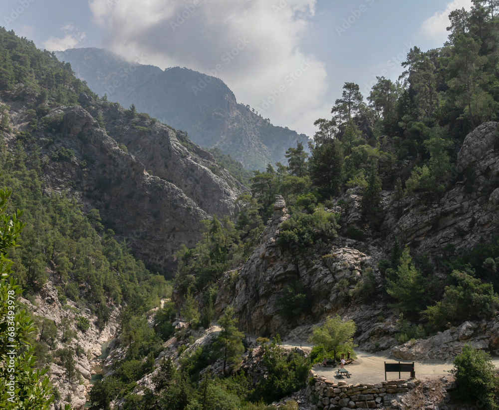 Panoramic view of the Goynyuk Canyon. A small mountain stream runs through a wide rocky gorge. The steep slopes are covered with Mediterranean forest. A recreation area area by the road.