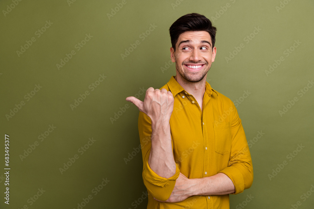 Portrait of nice positive man beaming smile look indicate thumb finger empty space isolated on khaki color background Portrait of nice positive man beaming smile look indicate thumb finger empty space isolated on khaki color background