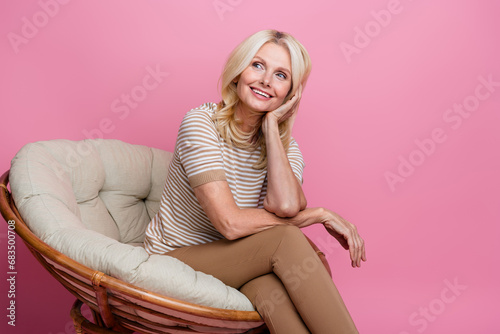 Portrait of peaceful minded lady sit comfy chair hand touch cheek look empty space contemplate isolated on pink color background