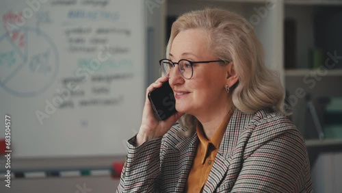 Beautiful middle-aged businesswoman smiling pleasantly while talking on phone photo