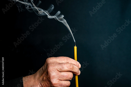 An elderly man, his hands are wrinkled. Holds a church candle, smoke.