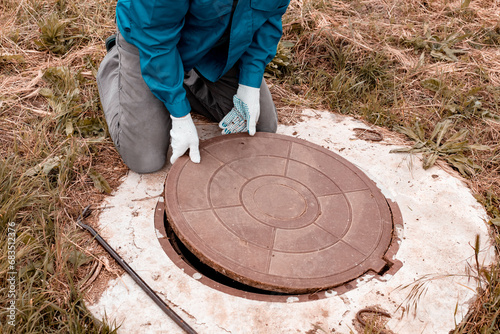 A worker lifts the manhole cover on a well for inspection and maintenance. Plumbing work in rural areas photo
