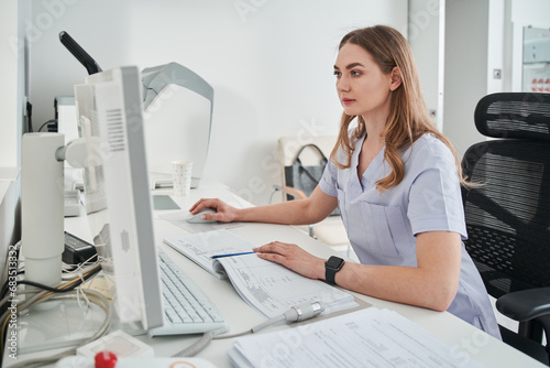 Focused lady nurse working computer while sitting at her workplace photo