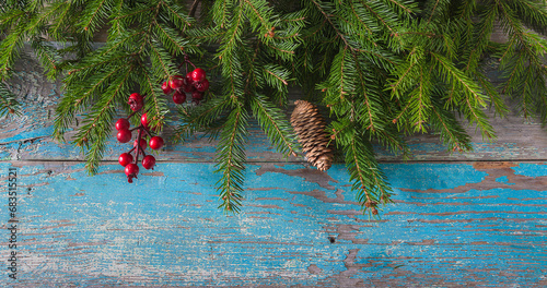 Frame of fir branches and berries on the old blue paint wooden background; Christmas holliday greeting card