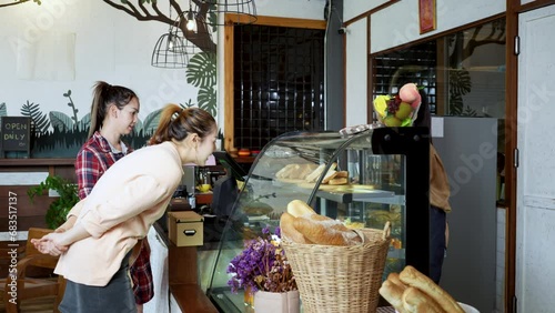 Tow Asian women customer buying cake in bakery and coffee shop.  Pretty female seller in apron sell sweet in bakehouse. Small business, shopping concept.