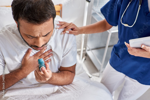 african american nurse helping her indian patient with asthma inhaler in his hospital ward