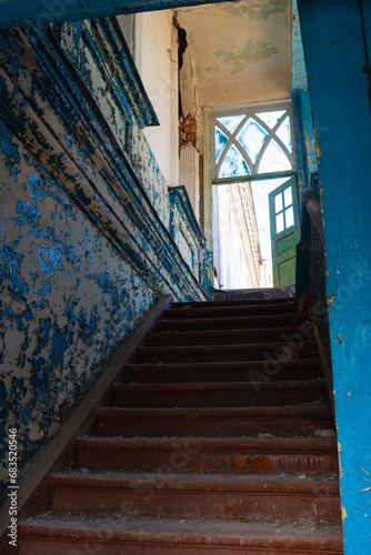 An old abandoned red wooden staircase in a crumbling building with blue walls and a beautiful window