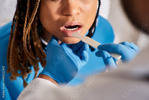 cropped view of doctor checking up throat of his young african american female patient  healthcare