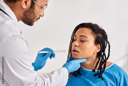 young ill african american woman in hospital ward having doctor check up of throat, healthcare
