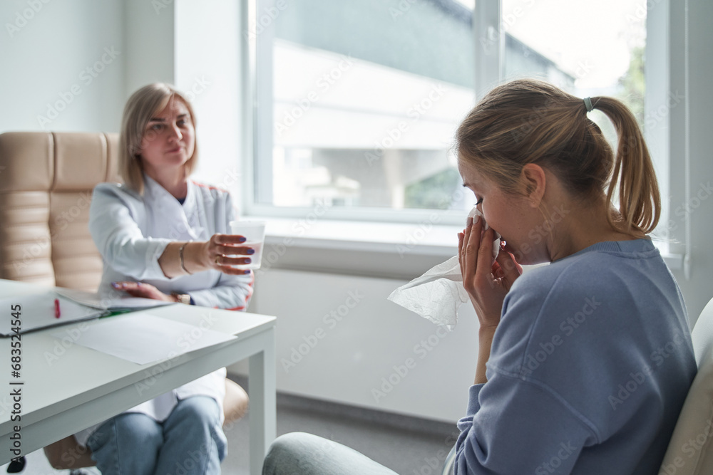 Friendly psychotherapist giving glass of water to crying patient woman Friendly psychotherapist giving glass of water to crying patient woman