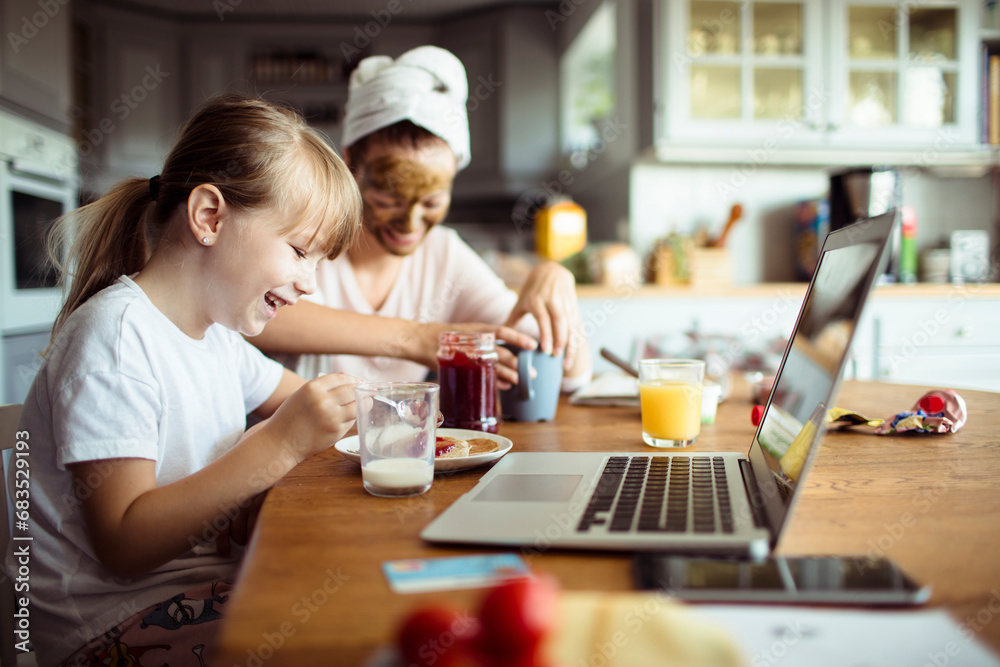 Little girl using laptop during breakfast in the kitchen with mother