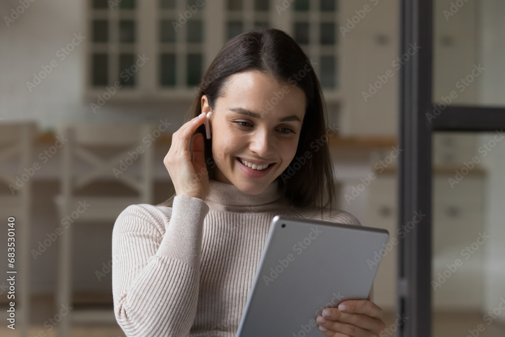 Beautiful young woman wear wireless earphones use digital tablet at home, close up, spend time on internet, watch video vlog, enjoy videocall talks via application. Modern tech, fun, leisure concept Beautiful young woman wear wireless earphones use digital tablet at home, close up, spend time on internet, watch video vlog, enjoy videocall talks via application. Modern tech, fun, leisure concept