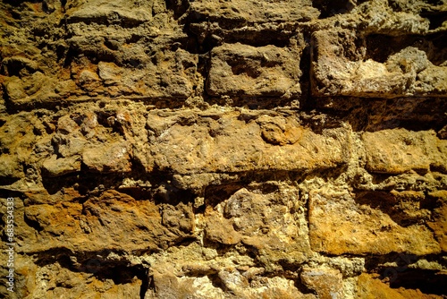 Close-up outdoor view of part of an ancient stone wall with a textured surface. An abstract image of a brown cemented, durable facade. photo