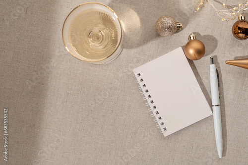Planning goals for New Year, making a wishes. Open blank notebook and pen on table background, wineglass with sparkling wine, Christmas ornaments, natural shadows. Flat lay, copy space