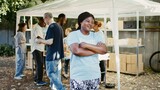 Enthusiastic black female volunteer, ready to provide humanitarian aid at a charity food distribution event. Multiethnic charity workers handing out free food to homeless people. Side-view, portrait.
