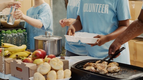 Multiethnic people in blue t-shirts, assembled outside to hand out food donations and help the homeless and hungry. Focus on volunteers serving free, freshly prepared meals to needy individuals.