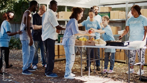 At charity food drive, volunteers share provisions and food with the homeless. Young people offer their time to feed the hungry among less fortunate, exhibiting the spirit of volunteerism. Handheld photo
