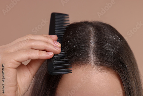 Woman with comb examining her hair and scalp on beige background, closeup. Dandruff problem