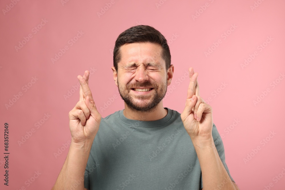 Emotional man crossing his fingers on pink background Emotional man crossing his fingers on pink background