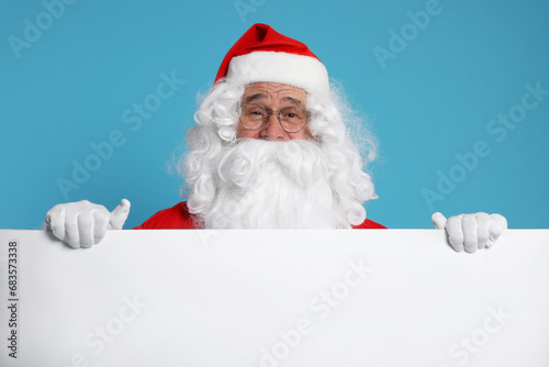 Santa Claus holding blank poster on light blue background. Space for text