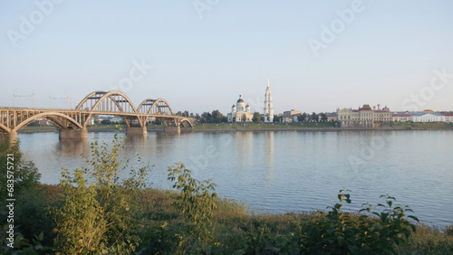 Beautiful bridge crossing wide river. Creative. City with a big church and green bushes.