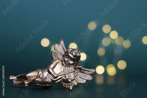 visao frontal de enfeite natalino em forma de  anjo barroco dourado tocando violino, com foco seletivo em fundo verde azulado e luzes desfocadas estilo Mockups photo