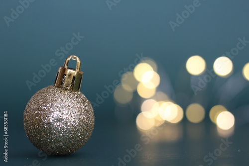 bola de natal dourada em primeiro plano a esquerda da foto com foco seletivo em fundo azul esverdeado e luzes desfocadas em composicao estilo Mockup photo