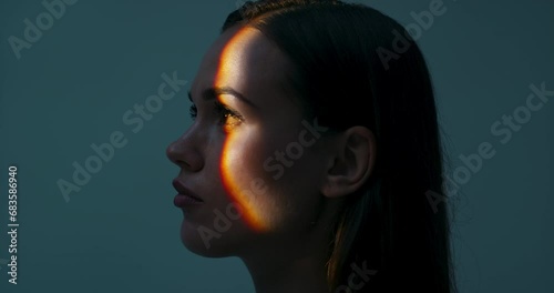 Young female in profile standing in studio isolated in bright light looking up playing with light dansinc with hands. Multicolour future of advertisement concept futuristic time.