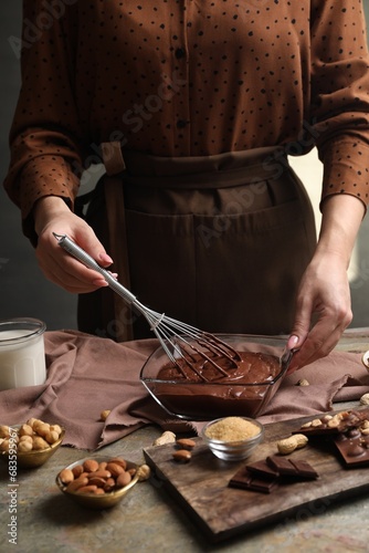 Woman mixing delicious chocolate cream with whisk at grey textured table, closeup