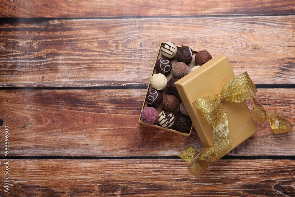 Open box with delicious chocolate candies on wooden table, top view. Space for text Open box with delicious chocolate candies on wooden table, top view. Space for text
