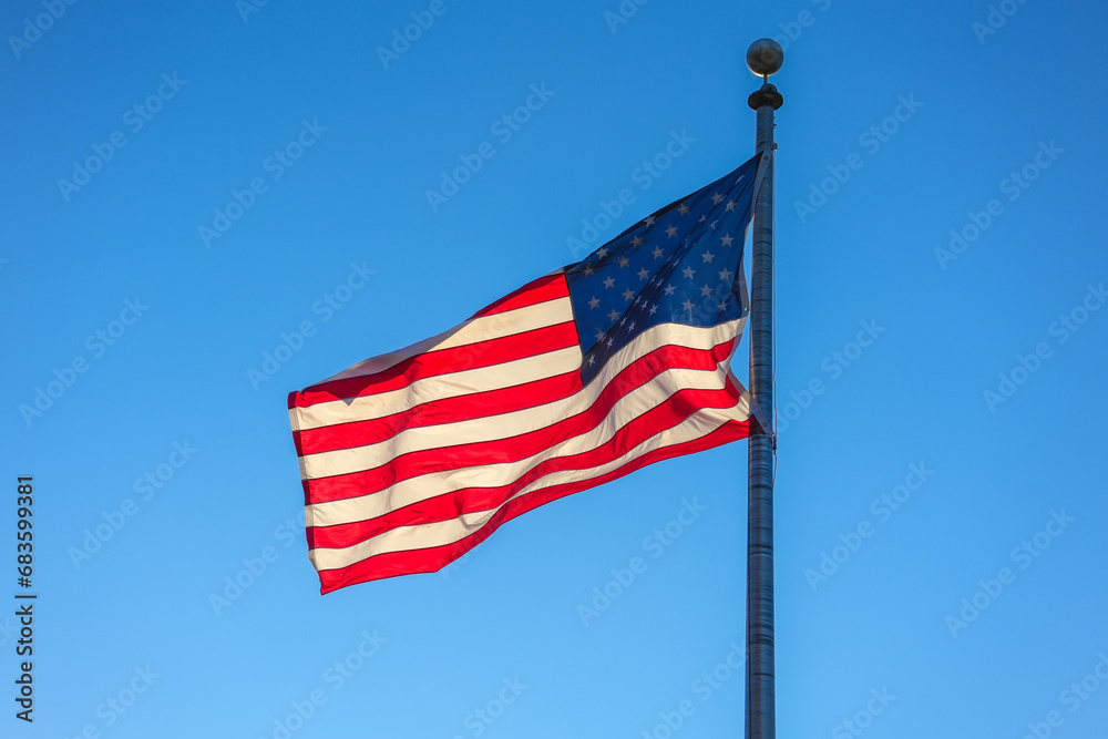 Fototapeta premium waving USA flag on pole against blue sky