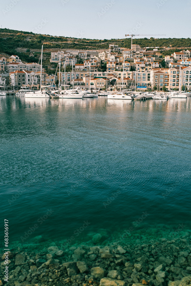 Rocky bottom of the clear Lustica Bay with moored yachts against the backdrop of colorful villas. Montenegro