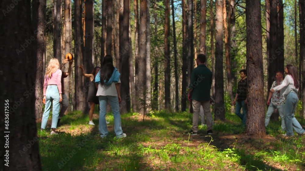 Fototapeta premium People play volleyball in forest. Stock footage. Tourists at recreation center play volleyball in forest. Vacationing people play ball in forest on sunny summer day