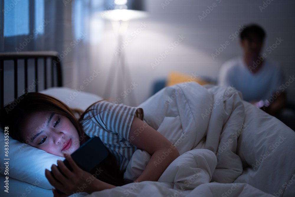 Asian girlfriend reading cartoon before watching Korean drama series while lie down and turn back in bed because sulk and angry boyfriend check online work on a sofa when bedtime night not go to sleep - obrazy, fototapety, plakaty 