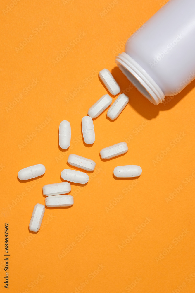 The white tablets were poured into an orange background from an unlabeled medicine bottle. Copy space for new drug advertising. Medical theme. The white tablets were poured into an orange background from an unlabeled medicine bottle. Copy space for new drug advertising. Medical theme.
