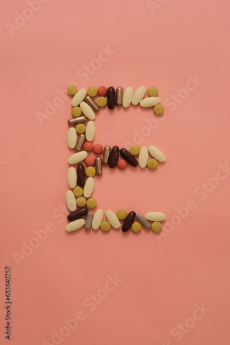 Top view of pills of different colors and shapes are arranged in an E shape on a pink background. Medical theme for medicine advertising. Copy space.